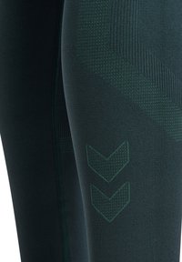 Ciemnozielone legginsy sportowe z teksturowanym wzorem, z prążkowanymi elementami oraz grafiką dwóch strzałek skierowanych w dół na nodze.