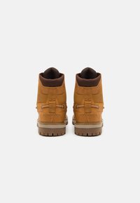 Botas de couro castanho com superfície texturizada, design de tornozelo alto, gola acolchoada e solas de borracha com um padrão de ranhuras. Detalhe discreto do logo.