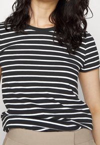 Camiseta de algodón a rayas en blanco y negro con cuello redondo y mangas cortas, que presenta un corte relajado y una textura suave.