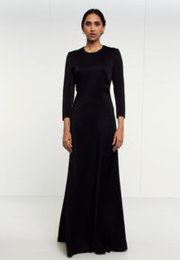 Mustade õhtukleit, millel on läikiv pealisosa ja pikad varrukad, valmistatud siledast kangast. Kleidil on põrandani ulatuv seelik ning minimalistlik kujundus.