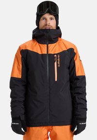 Giacca da snowboard nera e arancione con colletto alto, tasca sul petto e maniche a contrasto. Realizzata in materiale resistente alle intemperie.