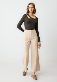 Body nero a maniche lunghe con scollatura asimmetrica e ritaglio, abbinato a pantaloni beige a gamba larga a vita alta e mocassini marroni.