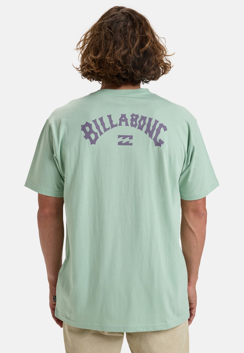 Lichtgroene T-shirt met korte mouwen en een groot paars "BILLABONG" logo en golfafbeelding op de achterkant. Zachte katoenstof, losse pasvorm.