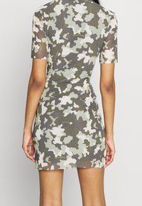 Kamouflage mini klänning med korta ärmar, i nyanser av grönt, grått och vitt. Slät textur med en åtsittande silhuett och rynkade detaljer.