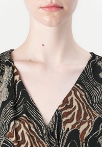 V-ringad plagg i ett abstrakt mönster av svart, brunt och beige. Har mjukt tyg med en lätt glans och knappar som detalj.