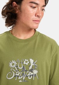 Olivově zelené bavlněné tričko s grafikou květin a abstraktních tvarů v bílé a šedé barvě, kulatým výstřihem a krátkými rukávy.