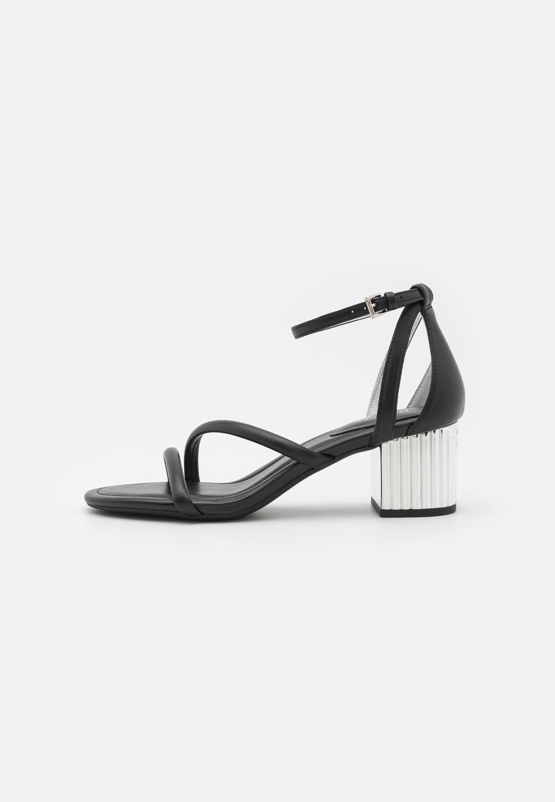 Sandale noire à brides avec bout ouvert, boucle à la cheville et talon bloc argenté métallique nervuré, sur fond blanc.