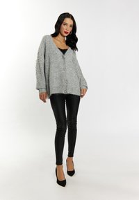 Cardigan tricotat supradimensionat, gri, cu accente de perle pe mâneci, având decolteu în V și închidere cu nasturi, asociat cu pantaloni skinny negri și tocuri.