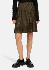 Gonna plissettata con un motivo leopardato marrone e nero, realizzata in tessuto leggero. Abbinata a scarpe nere con suola spessa.