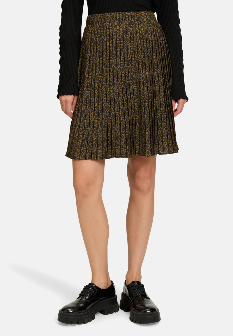 Gonna plissettata con un motivo leopardato marrone e nero, realizzata in tessuto leggero. Abbinata a scarpe nere con suola spessa.