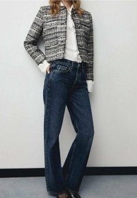 Czarna i biała krótka kurtka z tweedu z srebrnymi guzikami, zestawiona z wysokim stanem jeansami o prostych nogawkach w ciemnym niebieskim kolorze oraz czarnymi butami.