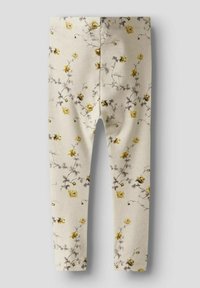 Ziedu legingi ar bēšīgu fona, uz kura ir dzelteni un pelēki ziedu raksti, izgatavoti no mīksta, elastīga auduma ar pieguļošu dizainu.