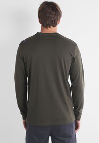 Chemise à manches longues couleur olive, fabriquée en tissu doux. Dotée d'un col rond et d'une petite étiquette sur l'épaule gauche. Design simple et ajusté.