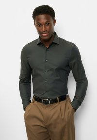 Dunkelgrünes, gemustertes Hemd mit Kragen und durchgehender Knopfleiste, kombiniert mit braunen Hosen und schwarzem Gürtel; glatte Stofftextur.