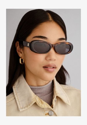 Barna teknős mintás napszemüveg ovális lencsékkel és karcsú kerettel. Bézs farmerdzsekivel és világosszürke garbónyakkal párosítva.