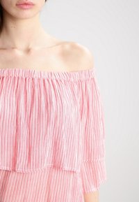 Top a spalle scoperte a righe in tessuto rosa chiaro e bianco. Presenta un collo elasticizzato e maniche corte svasate. Tessuto leggero.