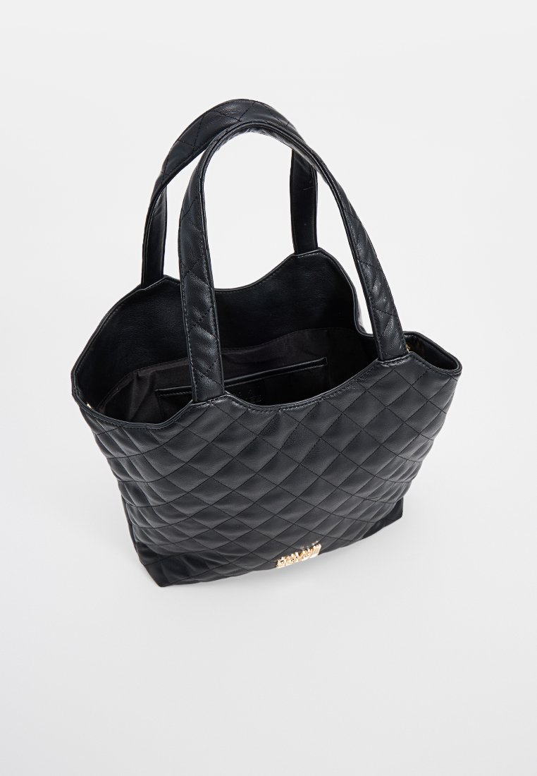 Svart kviltad läder tote-väska med två handtag och öppen topp som visar inre fickor, på en vit bakgrund.