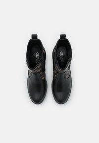 Černé kožené kotníkové boty s elastickými bočními panely, které mají hnědý vzor loga, špičatou špičku a design na nazouvání pro snadné obouvání.