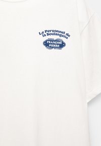Hvid bomulds T-shirt med blå tekst og grafik: "Le Personnel de la Boulangerie" med "François Pierre" emblem og dekorative accenter.