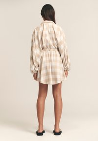 Karokleid in Beige und Weiß; verfügt über einen Hemdkragen, elastische Taille und lange Puffärmel sowie einen ausgestellten Rock.