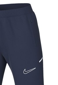 Pantaloni sportivi Nike navy con vita elastica, tasche laterali, dettagli testurizzati e un logo bianco vicino all'orlo. Tessuto liscio.
