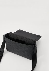 Svart veske med geometrisk mønster, laget av teksturert materiale. Den har klaffelukking og justerbar stropp, med et romslig indre.