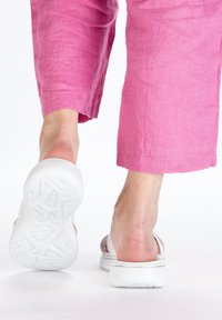 White sandals with a textured sole, showing an open back and thick straps. Worn with pink, loose-fitting, linen pants.