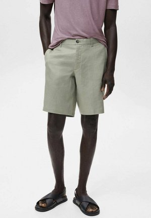 Pantaloni scurți din in verde deschis, cu o croială ajustată, buzunare frontale și bucle pentru curea, asortați cu sandale negre tip slide și un tricou mov pal.