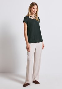 Top corto nero con ritagli nel neckline, abbinato a pantaloni larghi beige chiaro e scarpe slip-on marroni. Tessuto a trama liscia.