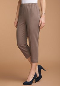 Bruine ribbroek met een elastische tailleband, taps toelopende pijpen en zijnaad. Gekleed met marineblauwe hoge hakken.