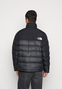 Giacca a vento nera con design trapuntato, parte superiore liscia e texture spazzolata sulle spalle, che mette in risalto il logo del marchio.