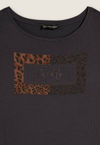 Camiseta gris oscuro con un diseño rectangular de estampado de leopardo en tres secciones con tonos marrones y la palabra "freddy" en una tipografía metálica.