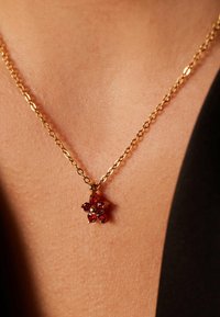 Gouden ketting met een bloemenhanger versierd met rode edelstenen, met een verfijnd ontwerp en een gladde metaaltextuur.