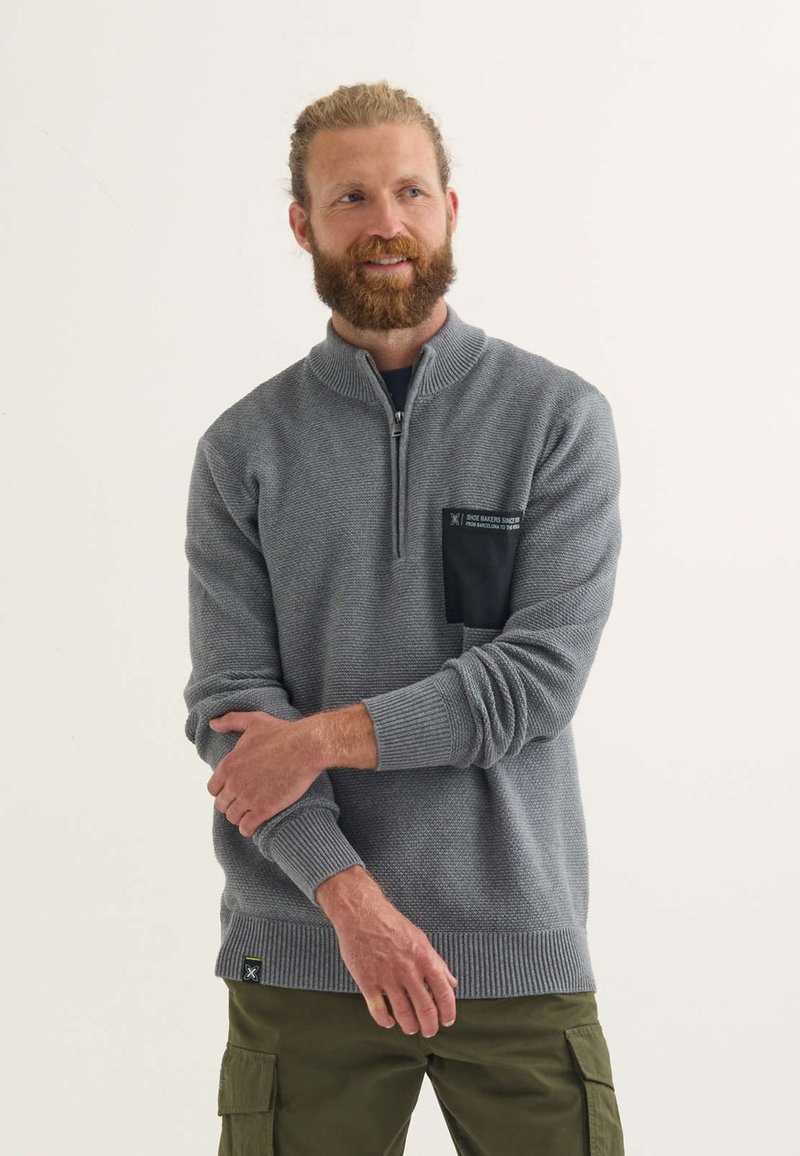 Pullover grigio a maglia con zip al collo, tessuto strutturato, polsini e orlo a coste, e una tasca sul petto nera con etichetta bianca.