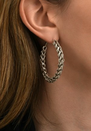 Boucles d'oreilles en argent avec un design tressé, mettant en avant des accents en métal tordu. La surface texturée met en valeur un savoir-faire complexe.