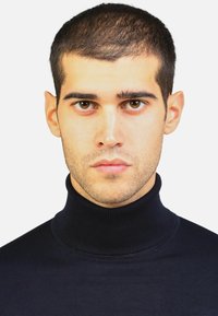 Maglione a dolcevita di un blu navy scuro realizzato in tessuto a costine, con un colletto alto e un design aderente, indossato da una persona con i capelli corti.