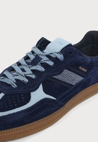 Basket en daim bleu marine avec des accents bleu clair, des lacets à motifs, une semelle en gomme et un marquage "ADIDAS" sur le côté et la languette.