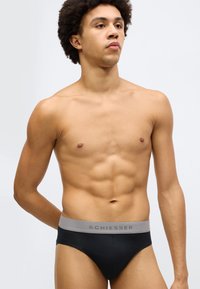 Fekete alsónadrág szürke rugalmas derékpánttal, amelyen a "Schiesser" márkanév finom betűtípussal szerepel, sima, rugalmas anyagból készült.