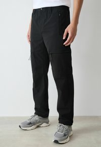 Schwarze Cargo-Hose mit Kordelzugbund, Reißverschlusstaschen und geradem Schnitt. Das Material wirkt leicht und glatt.