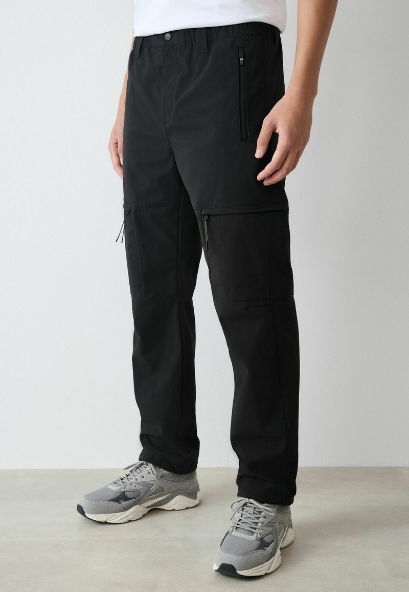 Schwarze Cargo-Hose mit Kordelzugbund, Reißverschlusstaschen und geradem Schnitt. Das Material wirkt leicht und glatt.