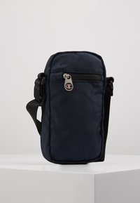 Granatowa torba typu crossbody z regulowanym czarnym paskiem, przednią kieszenią na zamek i suwakem z logo. Gładka tekstura i prostokątny kształt.