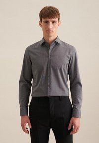 Grijze button-up overhemd van een licht gestructureerde stof, met lange mouwen, een standaard kraag en knopen aan de voorkant. Gecombineerd met donkere broek.