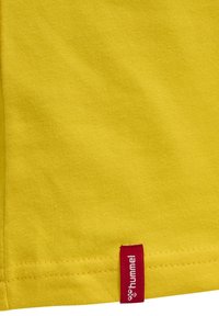 Gul bomullströja med en mjuk textur. Har en liten röd logotag på fållen som indikerar märket "hummel."