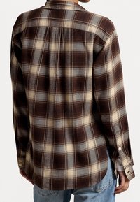 Brun och crème-rutig flanellskjorta med knäppning vid kragen, sänkta axlar och böjd nederkant. Mjuk textur med subtil lyster.