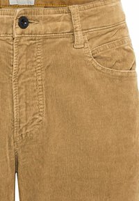 Pantalon en velours côtelé beige avec des fines côtes verticales, doté d'une poche avant et d'une fermeture à bouton unique. Texture douce avec des détails de couture visibles.
