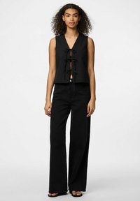 Juodas be rankovių viršus su giliu V formos iškirpimu ir trimis priekiniais raiščiais. Derinamas su juodomis, aukštu liemeniu, plačiomis džinsinėmis kelnėmis ir juodais sandalais.