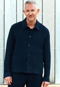 Marineblå tekstureret jakke med knaplukning foran, krave og lange ærmer; subtile vandrette striber og to frontlommer.