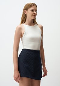 Top a righe bianche abbinato a una mini gonna blu con righe sottili. Tessuto liscio con un design aderente e una vita elasticizzata.