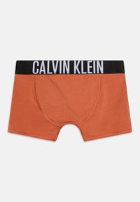 Oranžové bavlněné trenýrky s černým pasem, na kterém je bílým písmem napsáno "CALVIN KLEIN". Hladký materiál a přiléhavý střih.