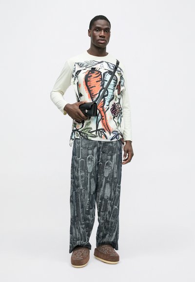 Λευκό πουκάμισο με μακριά μανίκια, διακοσμημένο με πολύχρωμα γραφικά καρότων και λουλουδιών, συνδυασμένο με φαρδιά σκουρόχρωμη παντελόνια με σχέδια και καφέ παπούτσια τύπου slip-on. Περιλαμβάνεται μαύρη τσάντα.